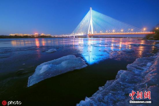 11月16日，黑龙江省哈尔滨市，进入流冰期的松花江，岸边堆满晶莹冰块，在松浦大桥、滨洲铁路桥的灯光映射下，一江璀璨如画。张澍
