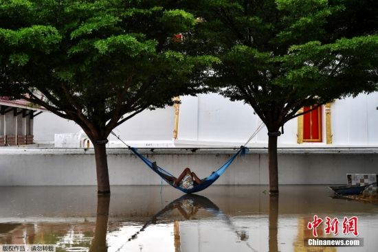当地时间9月29日，台风“电母”引发的强降雨在泰国多地形成内涝，当地居民只能借助船只在街道中通行。图为一名泰国民众“因地制宜”在吊床上休息。